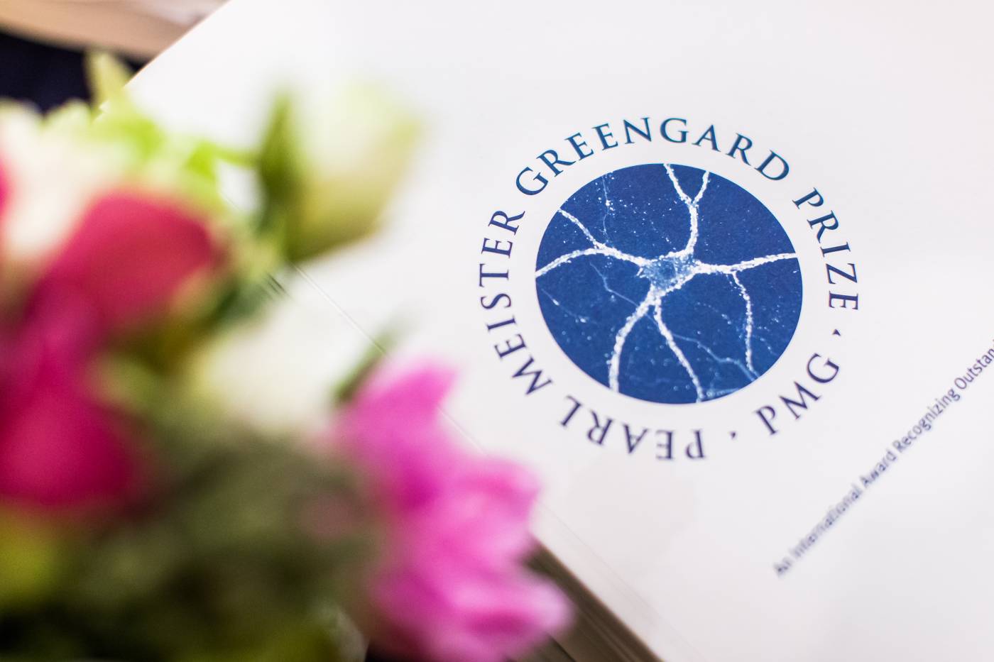 Pearl Meister Greengard Prize logo printed on paper, out of focus flower on left