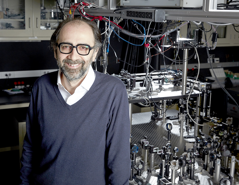 Alipasha Vaziri in a blue sweater stands next to light-beam microscope