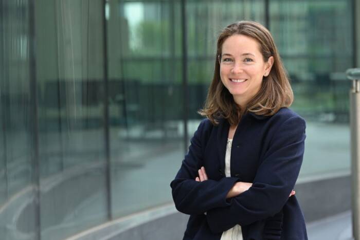 Dana Orange stands in a black coat before a glass wall