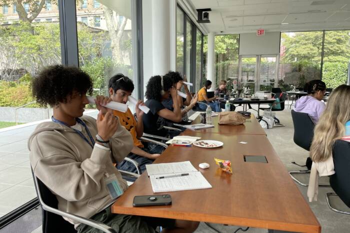 Four students looking through a rolled piece of paper in lecture