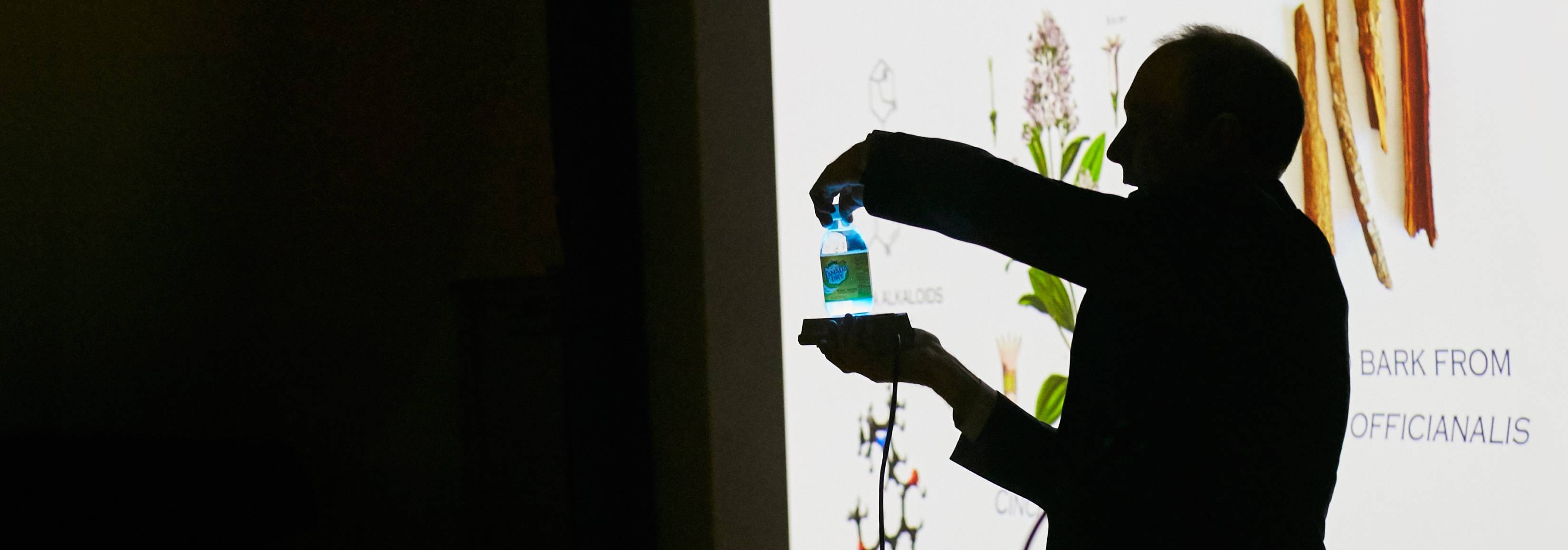 Silhouette of scientist shining blue light under liquid in bottle