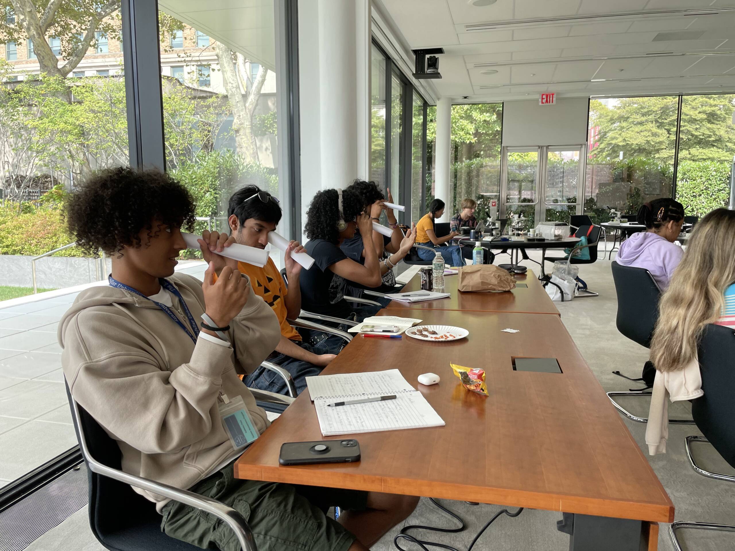 Four students looking through a rolled piece of paper in lecture
