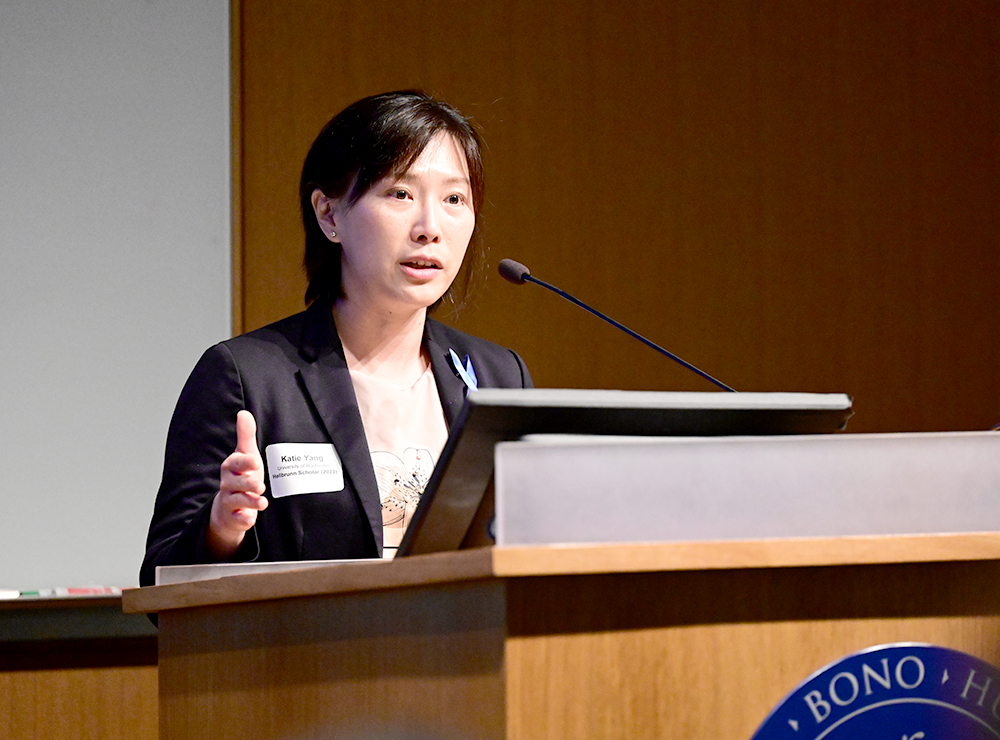 A woman with dark hair and a dark jacket speaks at a podium